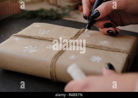 Frau Zeichnung auf Papier Schneeflocken Paket Weihnachten, Geschenk auf schwarzem Hintergrund. Weibliche Hände malen auf Geschenke für Winterurlaub. Weihnachten, Ne Stockfoto