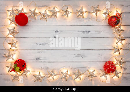 Eine Zeichenkette von Golden Star christmas lights und rote Christbaumkugeln, auf einem destressed woodern Hintergrund, Schaffung eines Rahmens um einen leeren Raum für Kopie Stockfoto