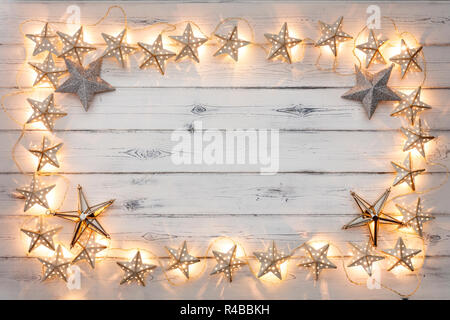 Eine Zeichenkette von Golden Star weihnachten Lichter und Sterne Flitter, auf einem destressed woodern Hintergrund, Schaffung eines Rahmens um einen leeren Raum für Kopie Stockfoto