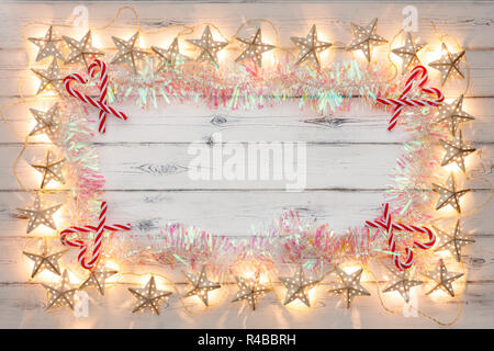 Eine Zeichenkette von Golden Star Weihnachtsbeleuchtung, Lametta und Candy sticks, auf einem destressed woodern Hintergrund, Schaffung eines Rahmens um einen leeren Raum für Cop Stockfoto