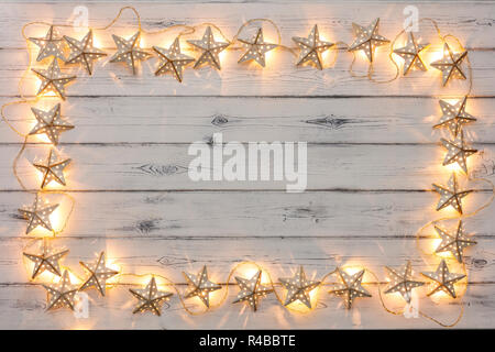 Eine Zeichenkette von Golden Star Weihnachtsbeleuchtung, auf einem destressed woodern Hintergrund, Schaffung eines Rahmens um einen leeren Raum für Kopie Stockfoto