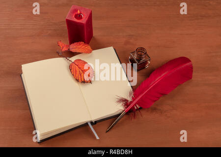 Gedichte zu schreiben. Ein Foto von einem roten Feder und Tinte gut und eine offene Notebook auf einem Schreibtisch aus Holz mit lebendigen Blätter im Herbst, und eine brennende Kerze Stockfoto