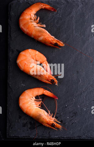 Blick von oben auf die frische Garnelen auf schwarzen Stein Schiefer mit Copyspace. Meeresfrüchte Zutaten Zubereitung. Stockfoto