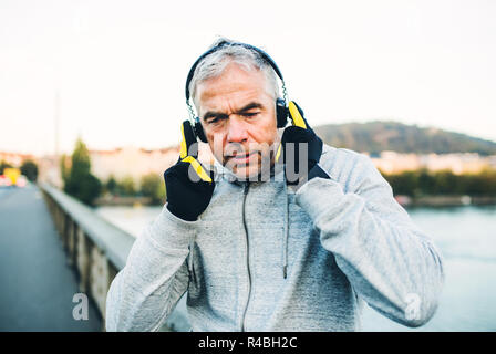 Reife männliche Läufer setzen auf Kopfhörer draußen in der Stadt. Stockfoto