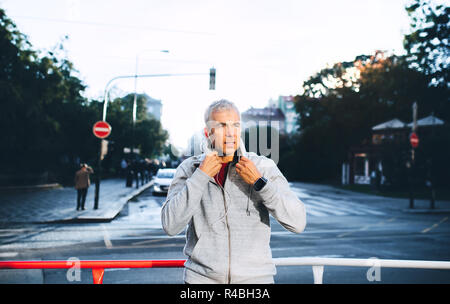 Ein Porträt eines aktiven reifer Mann mit Kopfhörern stehen draußen in der Stadt. Stockfoto