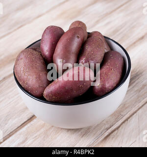 Nahaufnahme von einigen raw-Baby rote Kartoffeln in einem weißen ceramci Schüssel, auf einem rustikalen Holztisch gelegt Stockfoto