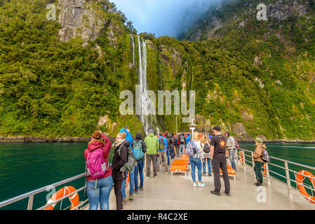 Gruppe von Menschen auf einem Kreuzfahrtschiff. Touristen in der Nähe von einem Wasserfall. Stirling fällt, Milford Sound Fjord, Fjordland, Neuseeland. Stockfoto