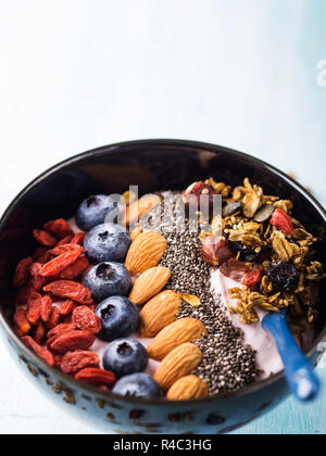 Joghurt Himbeer smoothie Schüssel mit Goji Beeren und Heidelbeeren, Mandeln, Chia Samen und Müsli auf Pastell türkis Holz- Hintergrund. Anlage b Stockfoto