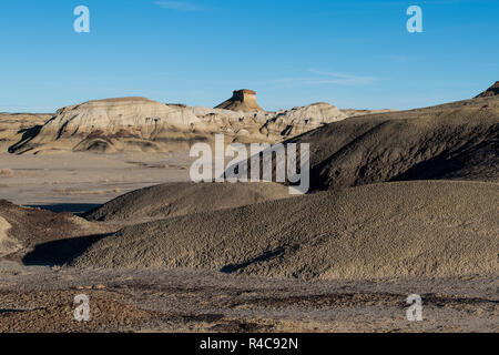 Ein entfernter Mesa erhebt sich über einer Wüstenlandschaft mit strukturierter, körnigen Hügel und Boden in der Bisti Badlands von New Mexico Stockfoto
