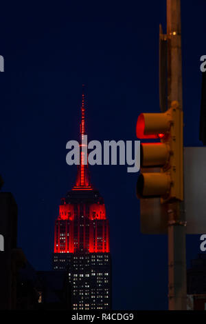 Eine rote Ampel im Vordergrund, während das ESB Empire State Building mit roter - oder kastanienbrauner - LED-Beleuchtung beleuchtet wird. Die Farbe des ESB sollte an das 175-jährige Bestehen der Fordham University erinnern. Stockfoto