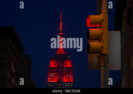 Eine rote Ampel im Vordergrund, während das ESB Empire State Building mit roter - oder kastanienbrauner - LED-Beleuchtung beleuchtet wird. Die Farbe des ESB sollte an das 175-jährige Bestehen der Fordham University erinnern. Stockfoto