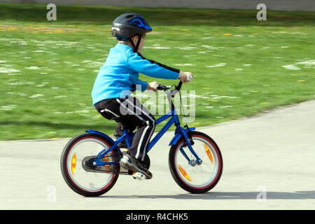 Kind auf einem Fahrrad an der asphaltierten Straße nach Verkehr Spielplatz - verschwommenes Schwenkmethode Stockfoto