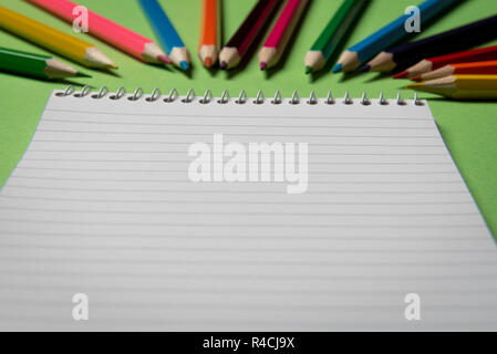 Spirale notebook leere Seite auf einem grünen Tisch mit vielen farbigen Holz- Bleistifte in Bokeh. Stockfoto