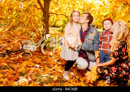 Portrait des Küssens Eltern und Kinder im Herbst Park sitzen am Nachmittag Stockfoto