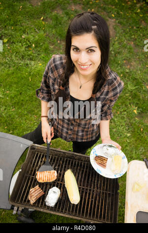 Hübsche Frau lächelnd Grillrost Steaks grillen Garten essen Stockfoto