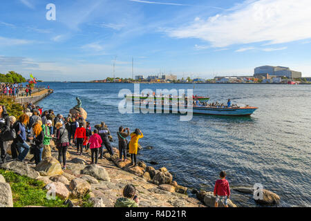 Touristen umgeben die Statue der Kleinen Meerjungfrau auf der Promenade Langelinie in Kopenhagen, Dänemark als Tour Boote schwimmen durch. Stockfoto