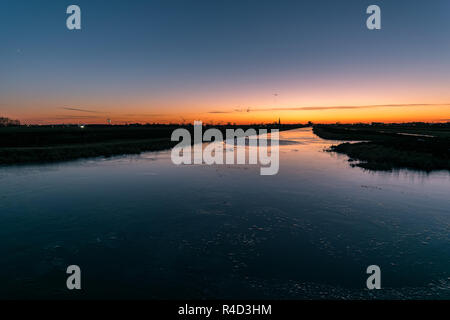 Bunt Dämmerung Himmel über den teilweise zugefrorenen Grachten in Holland. Schönen Schal blau und orange Farbe des Eis, durch Reflexion des Himmels verursacht. Stockfoto