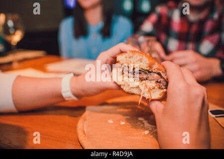 Mädchen, dass eine Gebissen ein Stück Burger in einer Hand. Mädchen mit lecker lecker fast food Cheeseburger. Das Konzept des Fast Food. Lecker ungesund Burger Sandwich in den Händen, Stockfoto