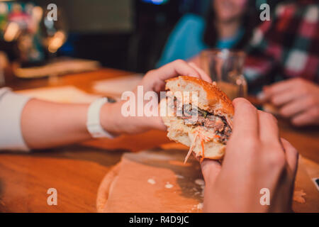 Mädchen, dass eine Gebissen ein Stück Burger in einer Hand. Mädchen mit lecker lecker fast food Cheeseburger. Das Konzept des Fast Food. Lecker ungesund Burger Sandwich in den Händen, Stockfoto