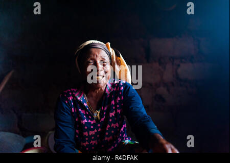 Douala Kamerun - 06. August 2018: Nahaufnahme der alte afrikanische Dame in ihren ländlichen Home Küche mit traditionellen Kleid gerade in die Kamera mit großen smi suchen Stockfoto
