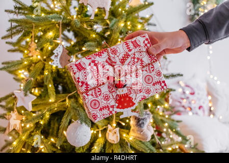 Die Hand eines Mannes hält ein Geschenk unter dem Baum. gemütliche Weihnachten Dekor Girlande bokeh. Neues Jahr 2019. Stockfoto