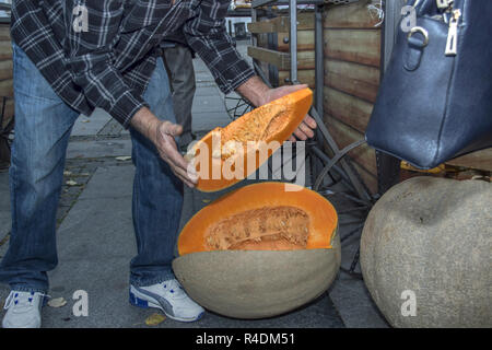 Zemun, Serbien, November 2018 - Ein greenmarket Verkäufer halten eine große Scheibe an reife Kürbis Stockfoto