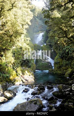 Wasserfall über große Felsen und grünen Bäumen, die sie umgibt, Milford Track Neuseeland Südinsel Stockfoto
