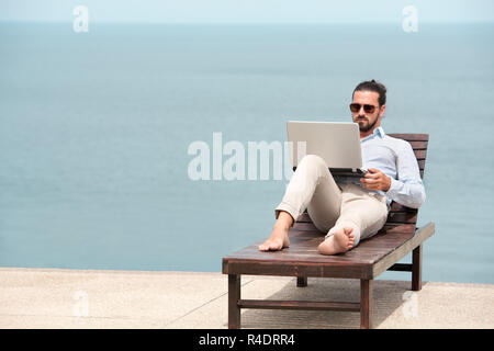 Geschäftsmann im Anzug mit Laptop am Strand Stockfoto