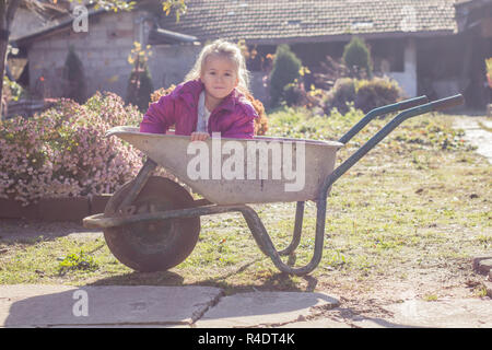 Gerne kleine Mädchen sitzen in Schubkarren Stockfoto