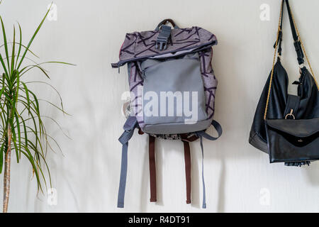 Lila Schule Rucksack an der Wand hängen - isoliertes Objekt mit weißem Hintergrund mit grünen Pflanze Neben es Stockfoto