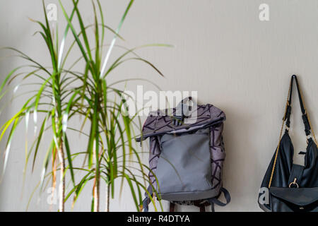 Lila Schule Rucksack an der Wand hängen - isoliertes Objekt mit weißem Hintergrund mit grünen Pflanze Neben es Stockfoto