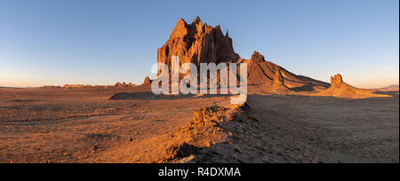 Panorama der Shiprock Felsformation über eine weite Landschaft, in dramatischen Morgenlicht steigend mit einer Straße Wicklung auf dem Weg zur Spitze Stockfoto