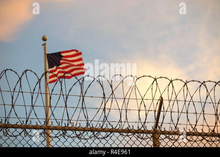 Guantanamo Bay auf Kuba. 16 Okt, 2018. Eine US-amerikanische Flagge weht hinter einem Stacheldrahtzaun im Wind. Die berüchtigten Camp hat jetzt fast 17 Jahren. 40 Insassen sind noch dort gehalten. (Dpa "Alterung der Gefangenen von Guantánamo Bay" vom 27.11.2018) Credit: Maren Hennemuth/dpa/Alamy leben Nachrichten Stockfoto