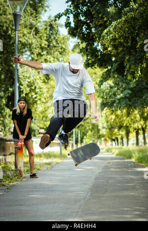 Junge führt eine skateboard Trick und das Mädchen sitzt und Uhren im Sommer Stockfoto