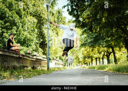 Junge führt eine skateboard Trick und das Mädchen sitzt und Uhren im Sommer Stockfoto