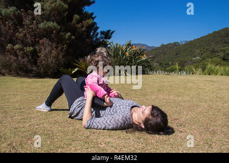 Mädchen sitzen auf den Bauch der Mutter in einem öffentlichen Park, Brasilien Stockfoto