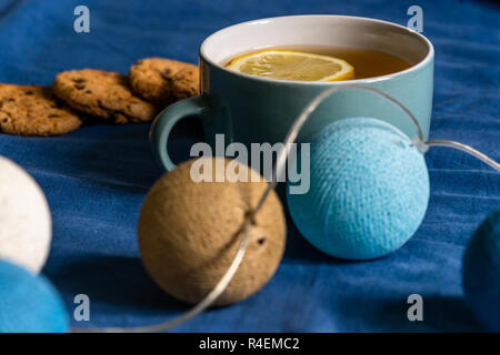 Tee mit Zitrone und Kekse mit Schokolade Verlegung auf Matratze - Weihnachten Dekoration Licht Kugeln Neben es Stockfoto