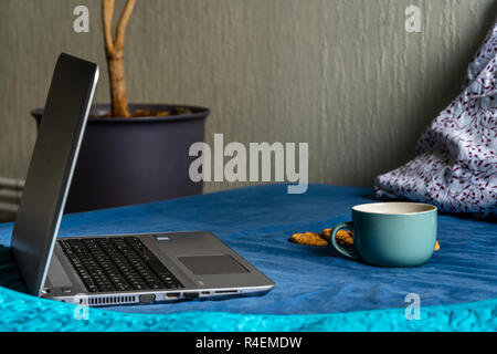 Tee mit Zitrone und Kekse mit Schokolade Verlegung auf Matratze - grau Laptop daneben, verschwommenes Türkis Hintergrund Stockfoto