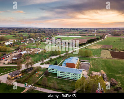 Antenne Drone Foto von einem Dorf mit Wiesen in schöner Frühling Farben in Abend Umgeben mit Sonnenuntergang über es Stockfoto