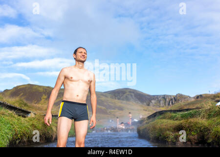 Junge glücklich Mann schwimmen Baden in heißen Quellen in Hveragerdi Reykjadalur im Süden Islands, golden circle, Felsen und Fluss Dampf, lächelnd Stockfoto