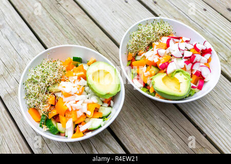 Zwei bunte große raw vegan Salat Schüsseln mit Alfalfa Sprossen, Avocado Hälften, gehackten Gurken, Orange Paprika, rote Rübe, Mittag- oder Abendessen, flach Stockfoto