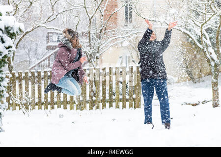 Junge Frau springen Mid-Air, Air, Spielen, das Werfen mit Schneebällen bei man im Winter Schneesturm, Sturm, zu Hause schneit, Haus Garten, Vorgarten, Hinterhof, Stockfoto