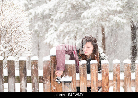 Junge Frau closeup stehend, öffnung Holz- Heim, Haus zaun Tor außerhalb, einen Vorgarten, Hinterhof, schweren Schneesturm, Sturm, Schnee, fallender sn Stockfoto