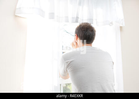 Zurück von einem jungen Mann, Mann, stehen, lehnte sich Arme, Hände gegen Kopf, heraus suchen, durch in weißen, hellen Zimmer des Hauses, Haus, Wohnung, sonnige l Stockfoto