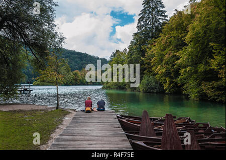 Zwei Leute sitzen auf einem Holzsteg über den See im Herbst und Meditieren während am Wasser. Plitvicer Seen, Kroatien Stockfoto