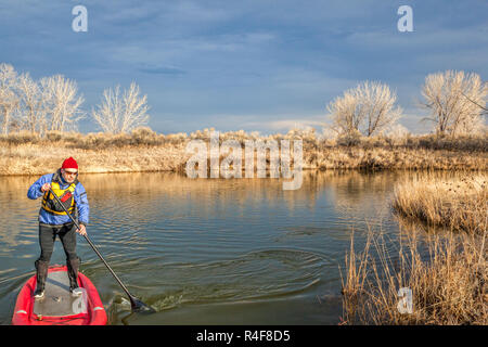 Älterer Mann ist das Paddeln eine aufblasbare Stand up paddleboard auf einem See im Herbst oder Winter Landschaft in Colorado Stockfoto