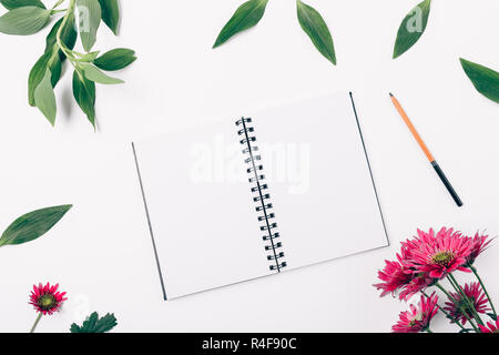 Flach öffnen leer Notizblock und Bleistift umgeben frische grüne Blätter und blüht rosa Blumen auf weißem Hintergrund, Ansicht von oben. Stockfoto