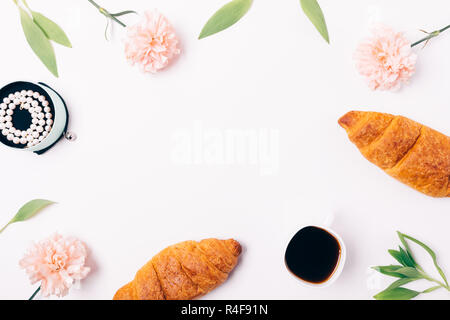 Florale flach Frame feminine Frühstück mit Croissants und Kaffee schwarz in der Nähe von Schmuck unter rosa Blüten mit grünen Blättern auf weißem Hintergrund, oben vie Stockfoto