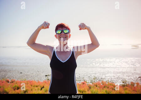 Ältere Frau mit Sonnenbrille Ihre Muskeln angezeigt Stockfoto