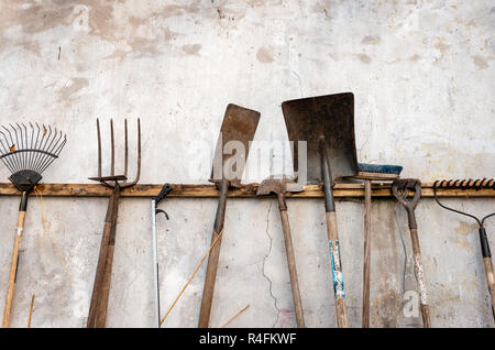 Eine Sammlung von verschiedenen gebrauchten rostigen Gartengeräten, die an verwitterten Wänden hängen. Stockfoto